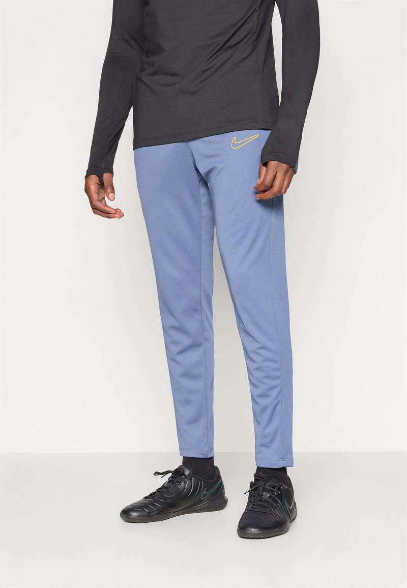 Nike treningsbukser i lyseblå, med slim fit, glatt tekstur, og en brodert logo i gull. Brukt med svarte treningssko.