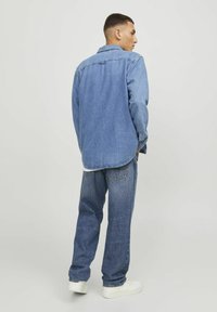 Jeanshemd und Jeans; hellblaues Material mit lockerer Passform. Das Hemd hat einen Kragen und knöpfbare Manschetten; die Hose verfügt über Gesäßtaschen und Umschläge.