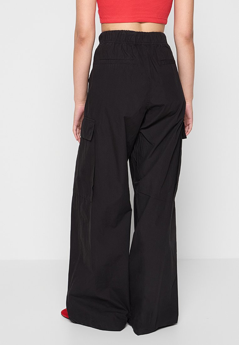 Pantaloni cargo neri a gamba larga realizzati in tessuto leggero, dotati di vita elasticizzata e tasche laterali per una maggiore praticità.