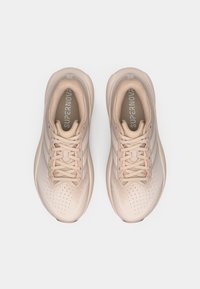 Ανοιχτό μπεζ παπούτσια τρεξίματος με επάνω μέρος από δίχτυ, διάτρητο σχέδιο, ροζ λεπτομέρειες στα κορδόνια και μαλακή σόλα. Λογότυπο στη γλώσσα.