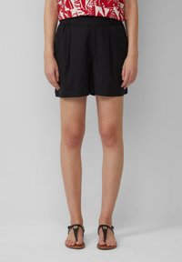 Shorts neri con una vestibilità comoda, dotati di pieghe e una vita elasticizzata. Abbinati a semplici infradito nere.