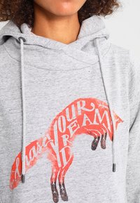 Szary hoodie z obszerna kapturem, z grafiką przedstawiającą czerwoną lisicę i napisem "Chase Your Dreams". Materiał mieszanki bawełny z sznurkami.