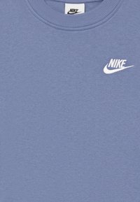 Svetlo modra crewneck majica s belim Nike logotipom vezenim na levem prsnem delu in Nike oznako na ovratniku.