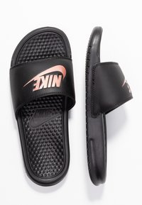 Black Nike slide sandals feature a textured footbed with raised dots, a smooth synthetic upper, and a metallic rose gold logo on the strap.