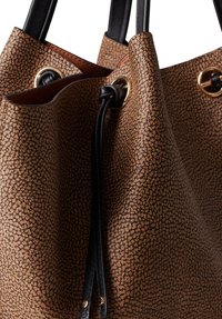 Borsa tote marrone con texture, caratterizzata da dettagli in pelle nera, occhielli in metallo dorato e chiusura a coulisse. La superficie presenta un motivo a puntini.