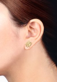 Goldene Blumenohrstecker mit filigranen Blütenblattdetails und einer strukturierten Oberfläche, die am Ohrläppchen einer Person positioniert sind.