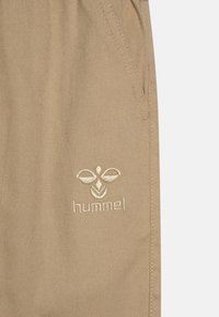 Beige trousers made of textured fabric with a slim fit. Features side pockets and an embroidered "hummel" logo in a lighter shade.