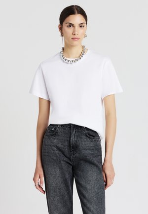 T-shirt bianco a maniche corte con vestibilità rilassata, abbinato a jeans scuri a vita alta. Una collana di perle argentate e orecchini a cerchio completano il look.