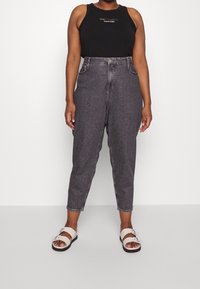 Černý tílko bez rukávů s nápisem „THIS IS LOVE“; šedé džíny s vysokým pasem; bílé sandály se dvěma nastavitelnými pásky.