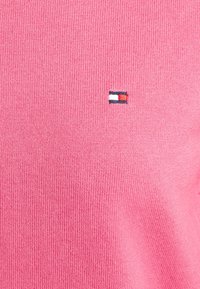 Pullover rosa in maglia con un piccolo logo ricamato in rosso, bianco e blu nella zona sinistra del petto. Tessuto leggero.