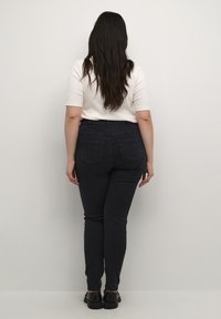 Jean skinny noir en denim avec taille haute, design à cinq poches et couture contrastante. Assorti à un haut blanc ajusté.