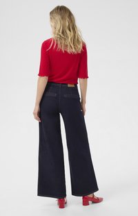 Laadukkaat tummansiniset leveälahkeiset farkut, joissa on kontrastiväriset ompeleet. Yhdistetty tiukkaan punaiseen paitaan, jonka koristeena on röyhelöhihoja, ja punaisiin pallean korkoisiin kenkiin.