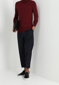 Maglione a collo alto bordeaux abbinato a pantaloni cropped blu navy e sneakers nere. Il maglione ha un orlo a coste e maniche aderenti.