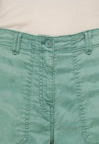 Mintgroene broek met een rits, een enkele knoopsluiting en opvallende stiksels bij de taille en zakken.