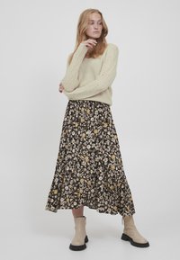 Strikket cremefarvet sweater med et tekstureret mønster, sat sammen med en sort blomsterkjol med gule og hvide blomster. Beige ankelstøvler fuldender looket.