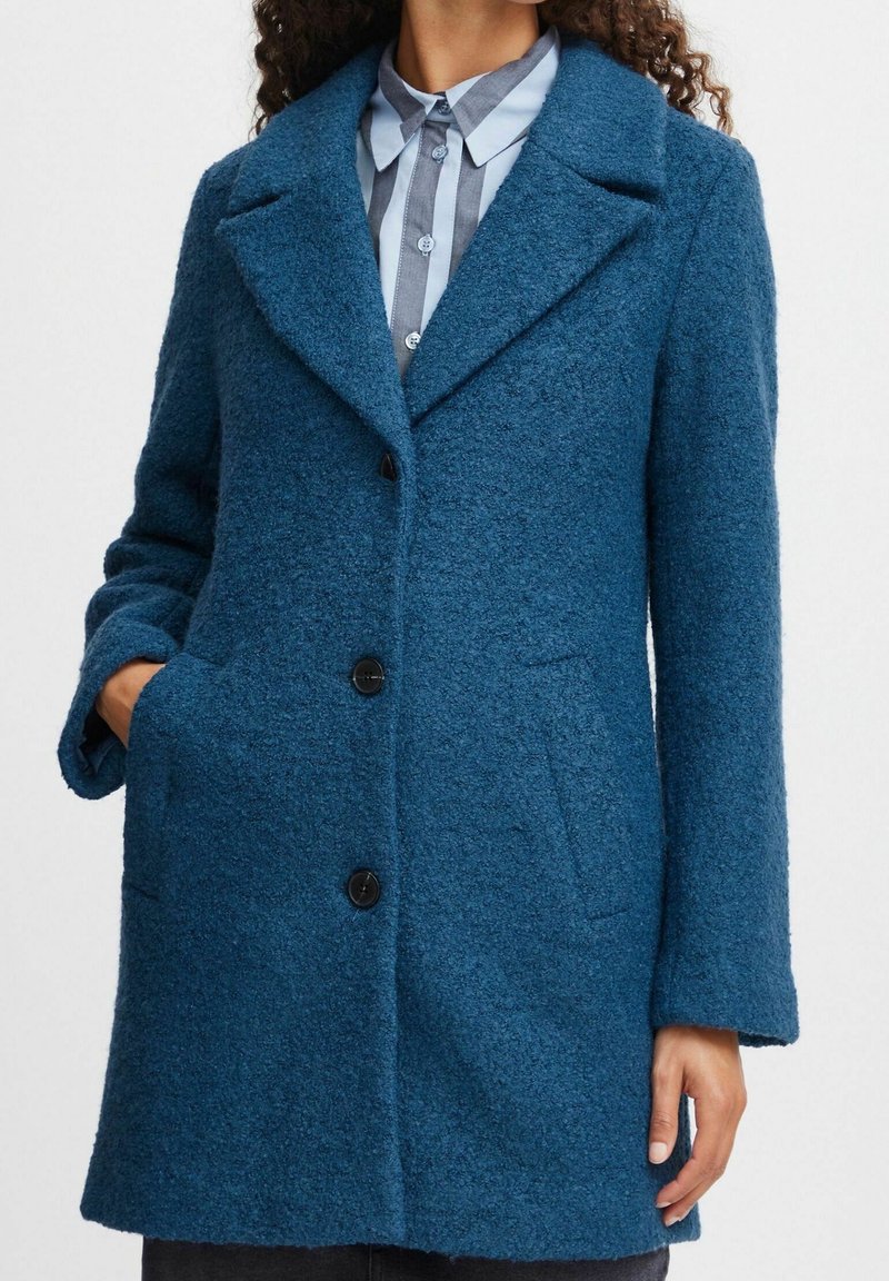 Cappotto in misto lana color verde teal con colletto a laccio, tre bottoni neri e due tasche laterali con finitura testurizzata.