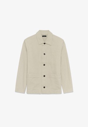 Veste en toile beige clair avec un col à revers, une fermeture à boutons sur le devant, et deux grandes poches plaquées. Elle présente des boutons noirs et un design minimaliste.