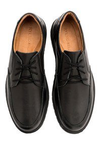 Scarpe in pelle nera con texture liscia, forma arrotondata e design con lacci. Presentano una soletta imbottita e un sottile dettaglio di cuciture.