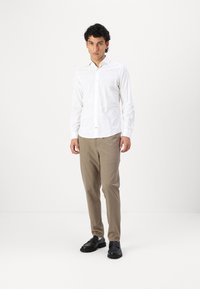 Cămașă albă cu mâneci lungi, cu un model paisley texturat, cu nasturi în față; asortată cu pantaloni bej deschis și pantofi negri slip-on.