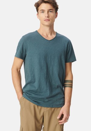 Teal V-Ausschnitt T-Shirt mit kurzen Ärmeln, aus leichtem Stoff. Hat eine weiche Textur und eine lockere Passform, kombiniert mit beigen Shorts.