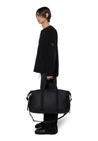 Borsone nero in materiale resistente, di grande dimensione, con manici doppi, tracolla staccabile e un brand discreto sul lato.