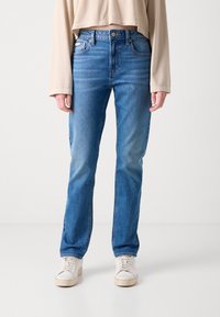 Blå denimjeans med rette ben, en falmet vask, fem lommer og metallknaplukking. Satt sammen med hvite sportsko.