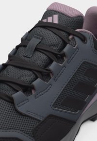 Lähikuva harmaasta ja mustasta urheilukengästä, jossa on mustat nauhat, verkkokangas, pehmustettu violetti kaulus ja Adidas-logo kielen päällä.