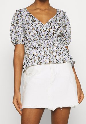 Bluse med blomstermønster i nuancer af lilla, grøn og sort, med V-udskæring, korte pufærmer og taljeret talje, kombineret med hvide denimshorts.