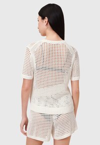 Hvid strikket sæt bestående af en løs, åbent vævet design med korte ærmer og ribbede detaljer, parret med matchende shorts.