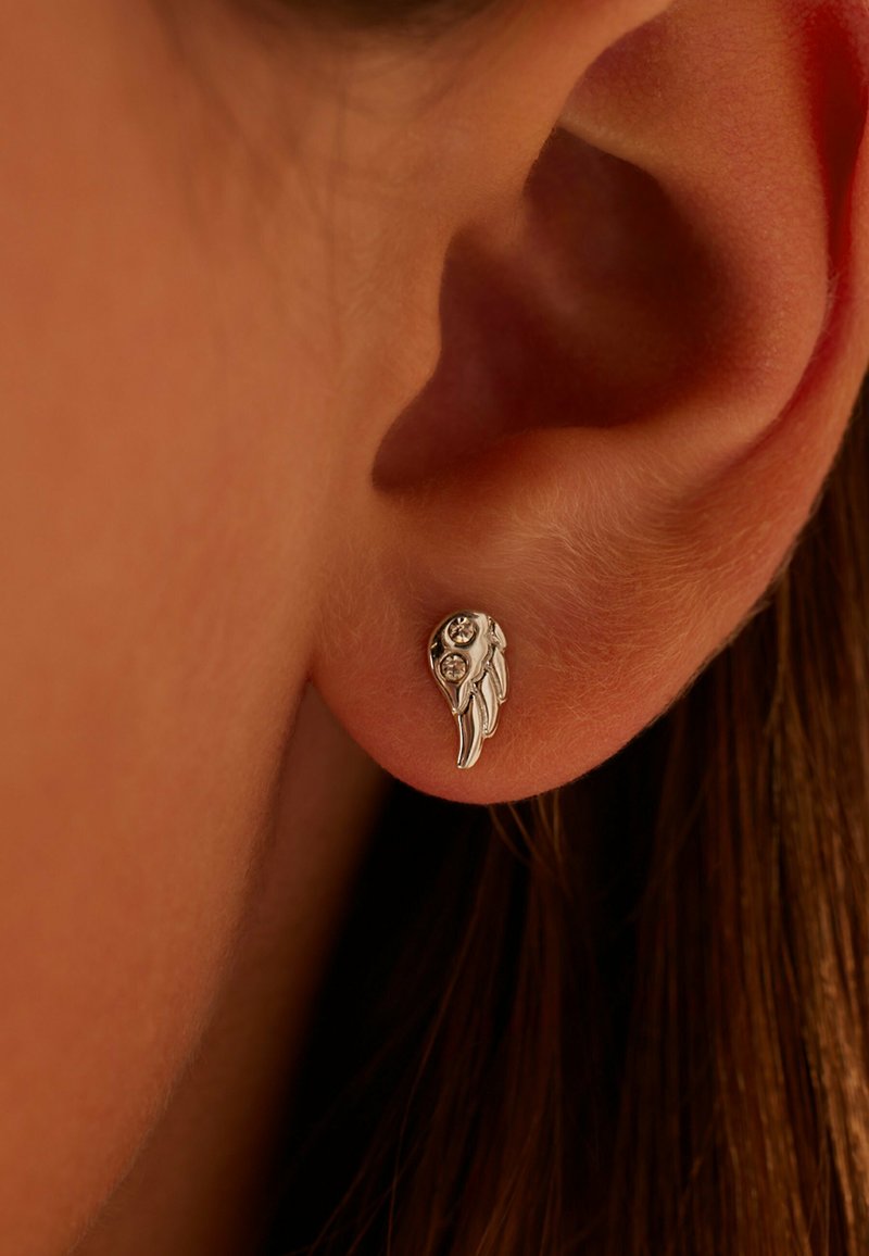 Sterling silver oorbel in de vorm van een vleugel met twee kleine heldere edelstenen, met gestructureerde details, bevestigd aan het oor van een persoon met bruin haar.