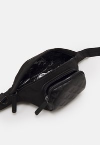 Musta olkalaukku, joka on valmistettu nailonista ja tekstuurisesta keinonahasta. Sisältää yhden pääosan, jossa on kiiltävä sisustus, sekä ylimääräisen vetoketjullisen taskun.