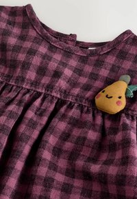 Robe à carreaux rose et noir avec une taille froncée et un col rond. Comprend un amusant patch de poire brodé sur la poitrine.