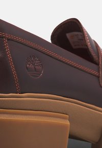 Ruskean nappanahkakengät, joissa on kontrastivärinen oranssi tikkaus, kohokuvioitu logo ja vaaleanruskea kumipohja, jossa on teksturoitu pinta.