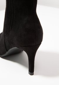 Czarne botki za kostkę wykonane z zamszu, z wąskim noskiem, wysokim obcasem typu stiletto i pionowym detalem zszycia na cholewce. Gładka tekstura.