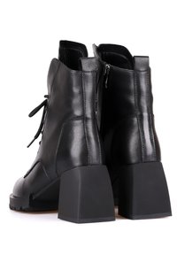 Bottines en cuir noir avec talons blocs, fermetures éclair latérales et lacets à l'avant, vues de dos sur un fond blanc.