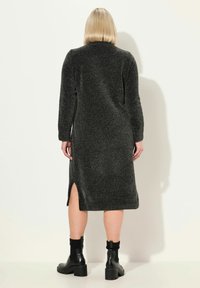 Robe en tricot gris foncé longue avec des manches longues, fente sur le côté et poignets côtelés. Associée à des bottines noires. Texture lisse, design minimaliste.