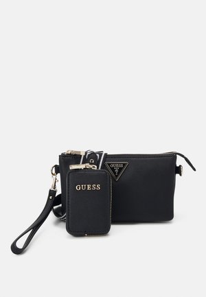 Petit sac bracelet noir Guess avec une petite pochette zippée détachable et une bandoulière rayée amovible sur fond blanc.