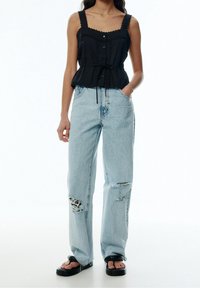 Haut péplum noir avec bordure en dentelle et boutons sur le devant, associé à un jean large bleu clair déchiré et des sandales noires.