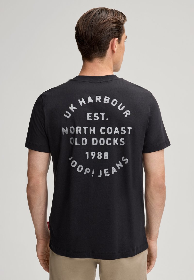 T-shirt en coton noir avec un imprimé graphique rond au dos comportant du texte en blanc : "UK HARBOUR EST. NORTH COAST OLD DOCKS 1988 JOOP! JEANS."