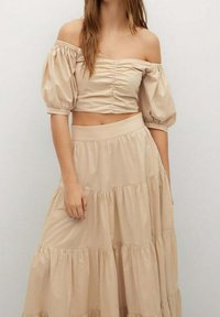 Toppi beige, joka on lyhyt ja olkaimeton, ja jossa on rynkytettyjä yksityiskohtia. Yhdistetty ilmavaan, kerrokselliseen maksihameeseen samassa värissä.