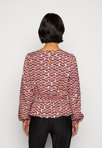 Musterbluse mit langen Ärmeln, die rot-, weiß- und navyfarbene Blumenmuster aufweist. Elastischer Bund und Rückenschlitzverschluss.