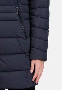 Marineblå pufferjakke med quiltet design, glat tekstur og en sidelomme med lynlås. Justerbar kant med et elegant udseende.