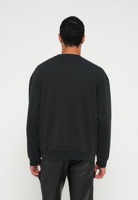 Sweatshirt preta com corte descontraído, gola redonda e punhos canelados. Material de algodão, design minimalista e sem padrões ou logotipos visíveis.