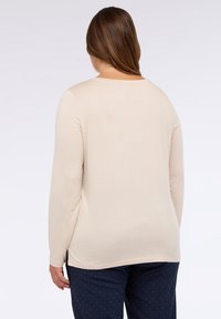 Beige Langarmshirt mit Rundhalsausschnitt, weichem Material und Seitenschlitzen, kombiniert mit navyblauen Pantalons mit Punkten. Einfaches und lässiges Design.