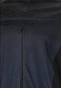 Veste de sport noire et bleu foncé avec une fermeture éclair verticale et le mot "ENDURANCE" près de la poitrine.