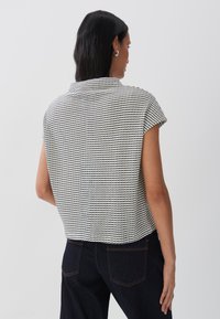 Camisetta a maniche corte con un motivo a griglia bianca e nera texturizzato, caratterizzata da un colletto e una vestibilità leggermente oversize. Indossata con pantaloni di denim.