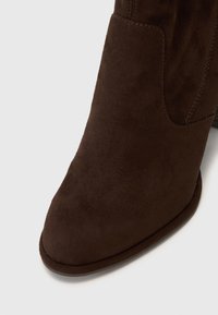 Bottine en daim marron avec un bout pointu, texture lisse et détails de couture latérale, dotée d'un petit talon empilé.
