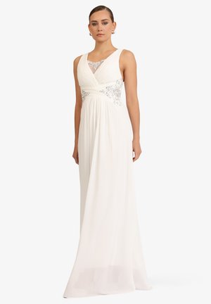 Woman wearing a white sleeveless floor-length gown with silver embroidery and lace detail on the bodice, standing against a plain background.