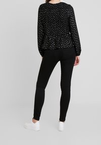 Black long-sleeve blouse with white polka dots, smocked back, and peplum waist, paired with black skinny jeans and white sneakers.