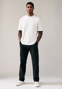 Weißes kurzärmeliges T-Shirt, schwarze Hose und weiße Sneaker. Das T-Shirt hat eine lockere Passform, die Hose ist mit einer flachen Vorderseite gestaltet.